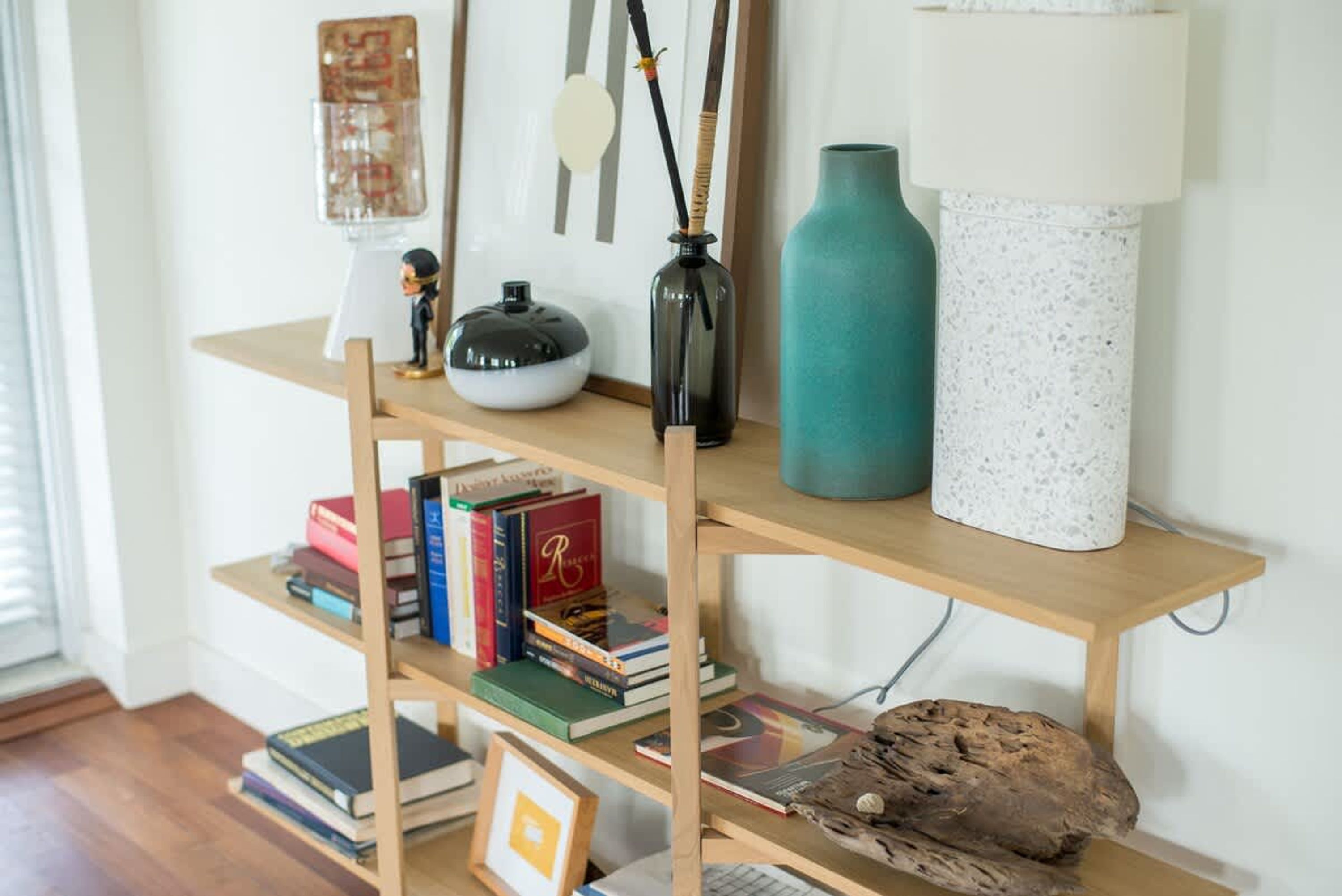 A wooden bookshelf with books, a black vase, a teal vase, and a white lamp.