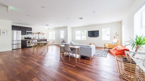 Un'ampia zona giorno con tavolo da pranzo, divano e poltrone. Si intravede in secondo piano una cucina con elettrodomestici moderni.
