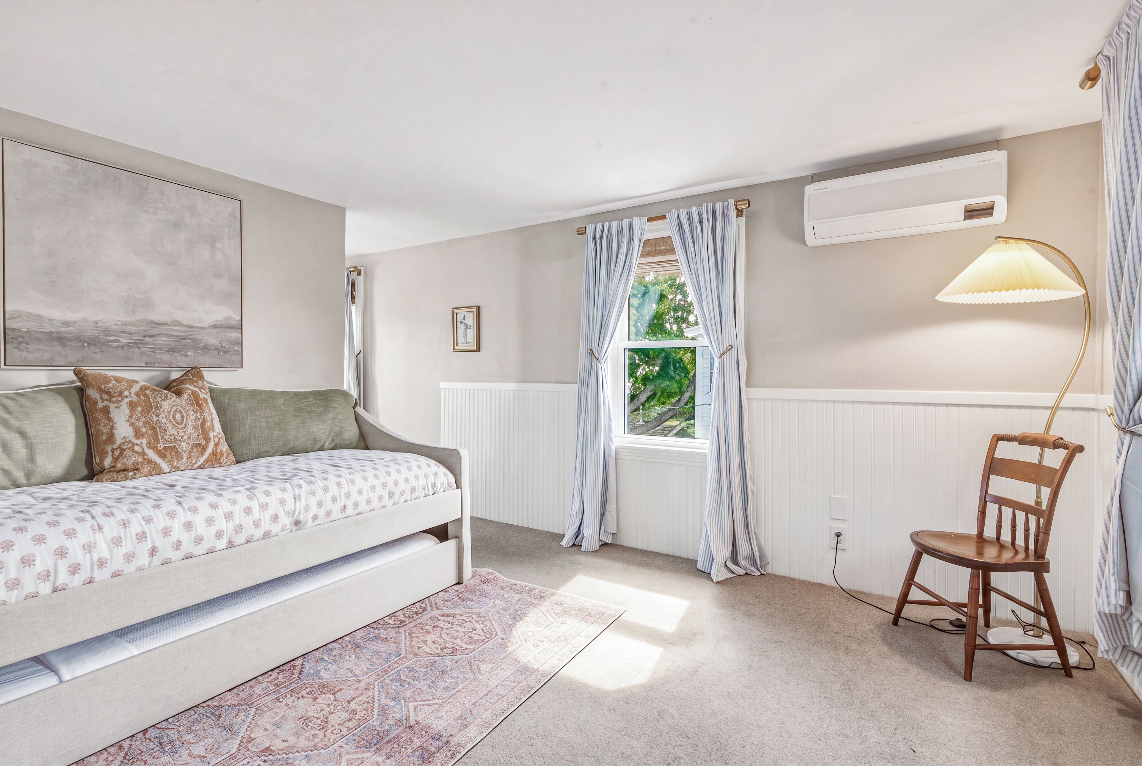 A bedroom with a bed, a chair, a window with curtains, a radiator, and a lamp.