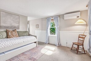 Un dormitorio con cama, una silla, ventana con cortinas, radiador y una lámpara.