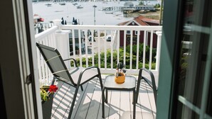 Un balcon avec deux chaises et une petite table, donnant sur une marina où sont amarrés des bateaux, et sur une côte lointaine.