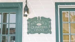 Un letrero para Admiral's Quarters Inn con un diseño vintage, ubicado sobre un ventanal con una puerta verde.