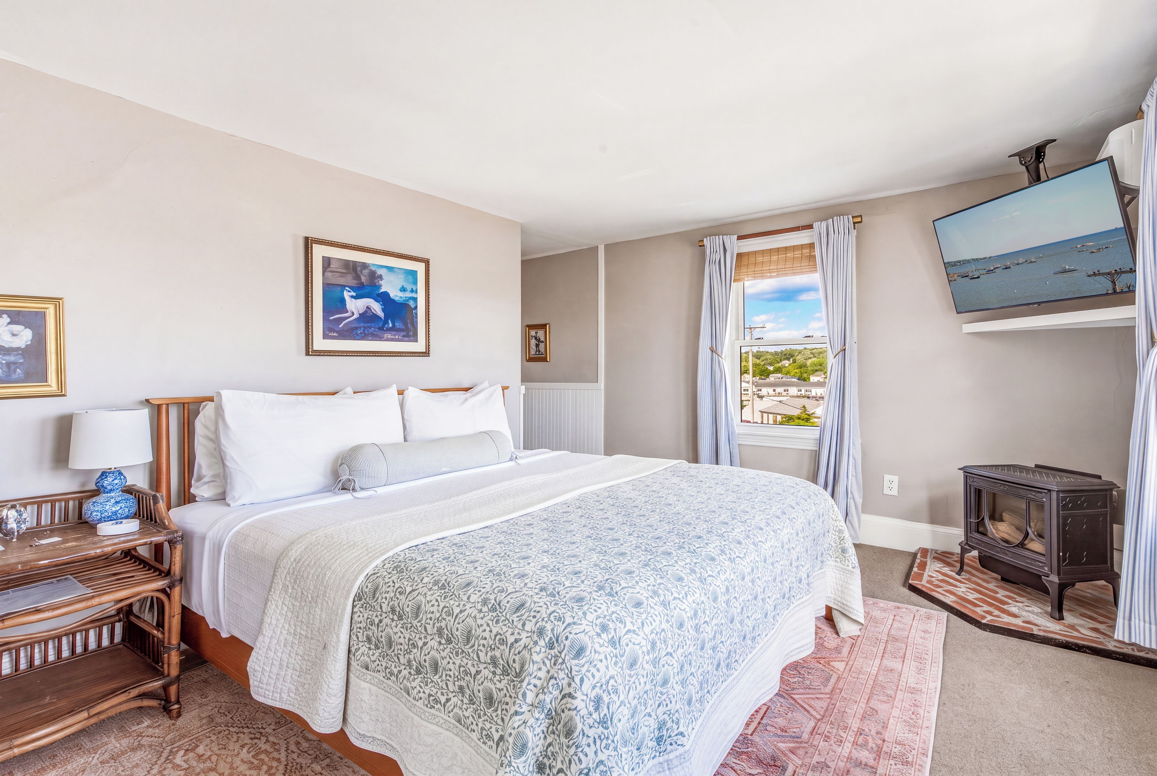 A bedroom with a bed, a nightstand, a lamp, a heater, a TV, and a view of the sea.