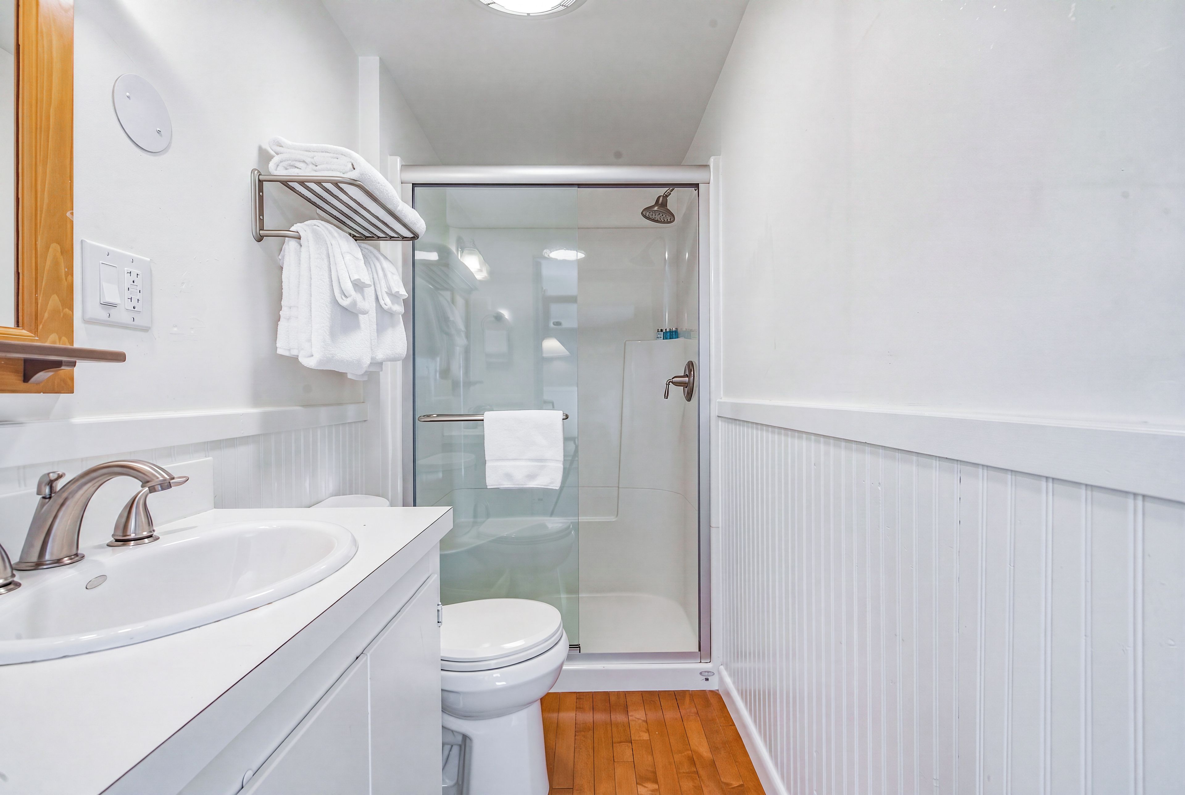 A bathroom with a white sink, a toilet, a glass shower enclosure, and a towel rack.
