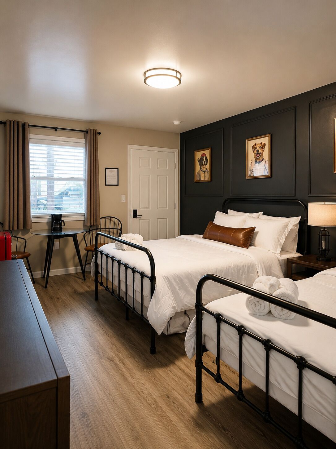 A hotel room with two beds, a desk, a chair, a window with curtains, and a door.