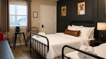 A hotel room with two beds, a desk, a chair, a window with curtains, and a door.