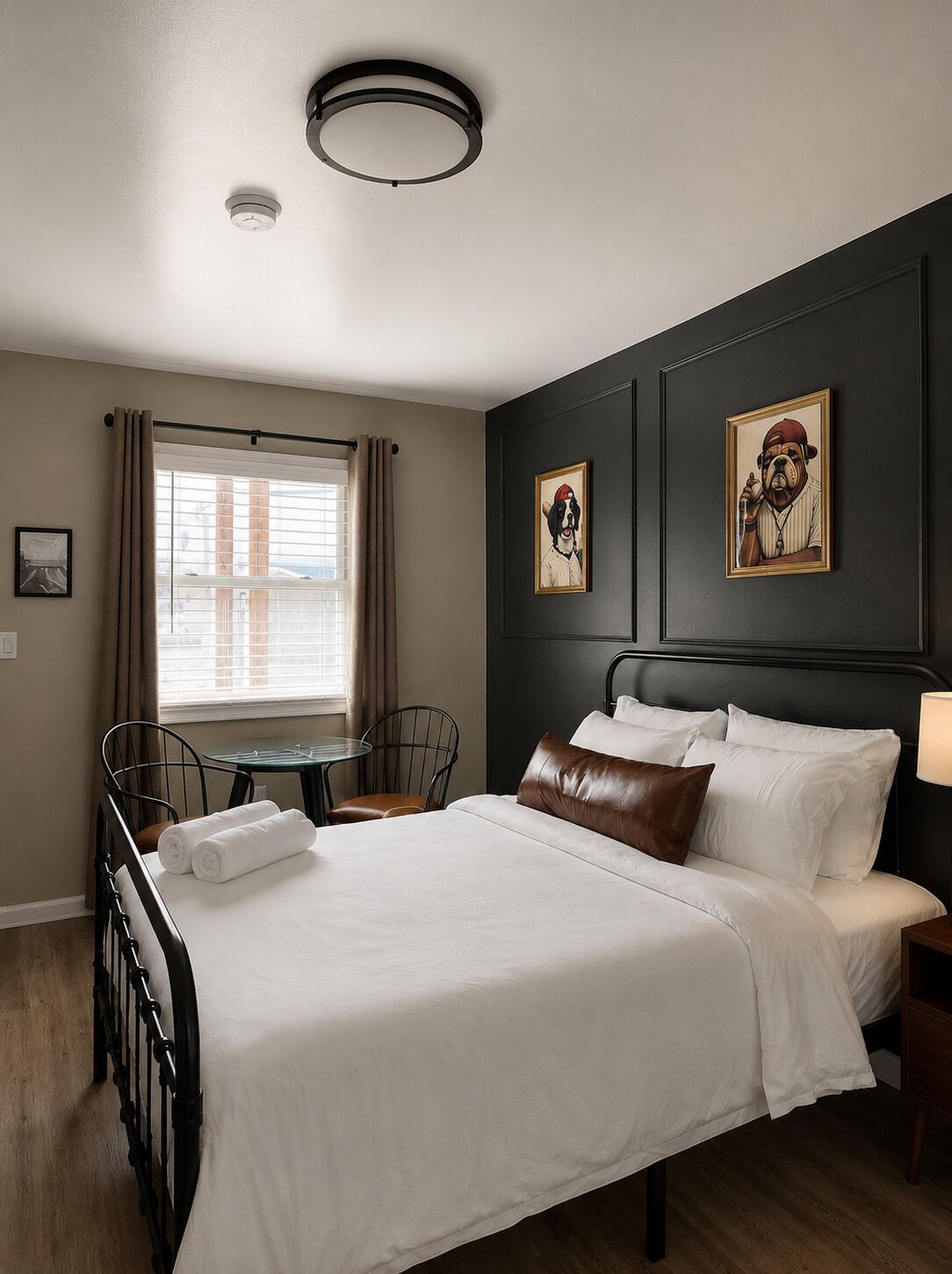 A hotel room with a bed, a table, a chair, and two framed pictures on the wall.