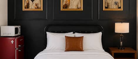 Een hotelkamer met een bed, een nachtkastje met een lamp, een rode apparatuur en drie foto's in lijsten aan de muur.