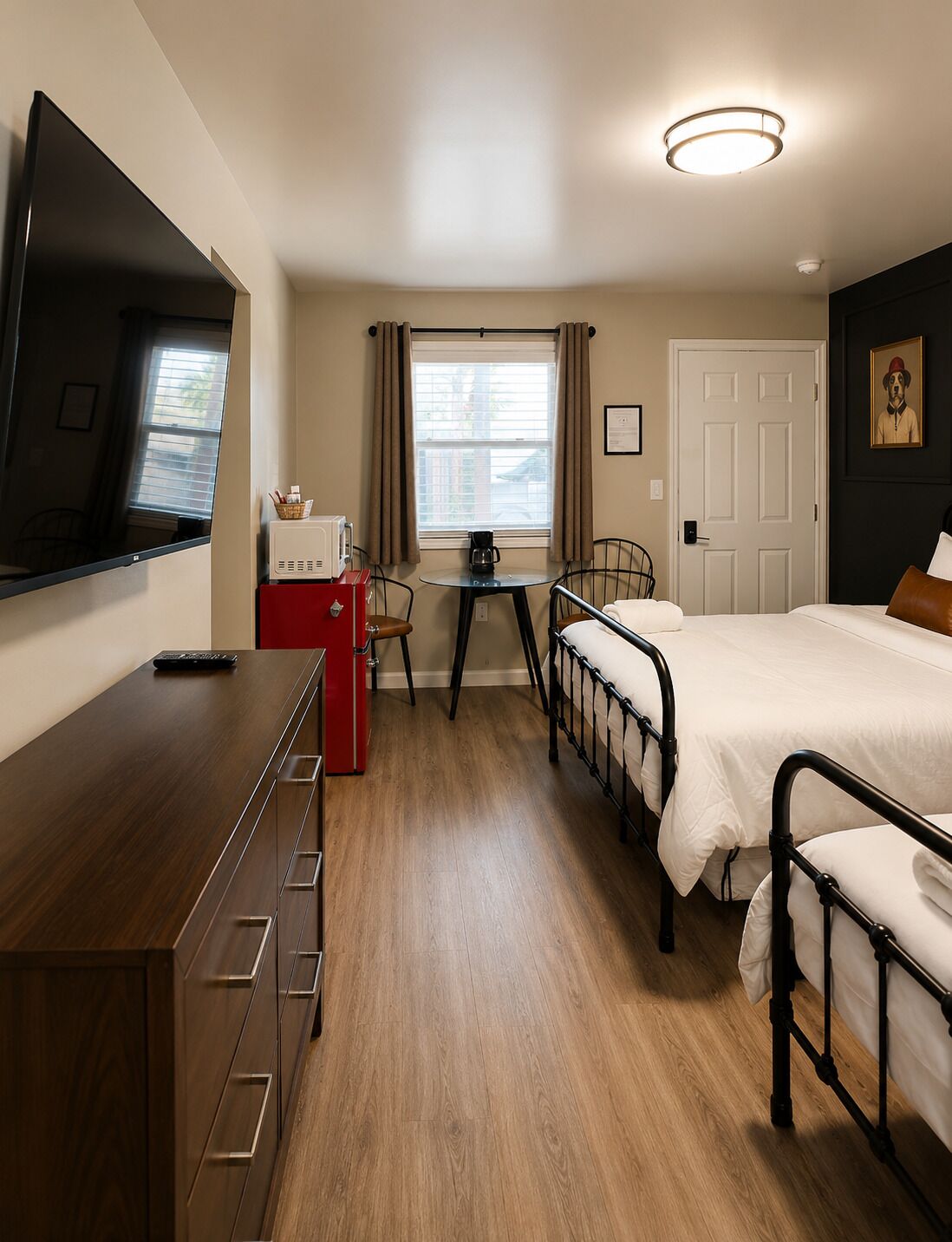 Una habitación de hotel con cama, escritorio, televisor, ventana con cortinas y puerta.