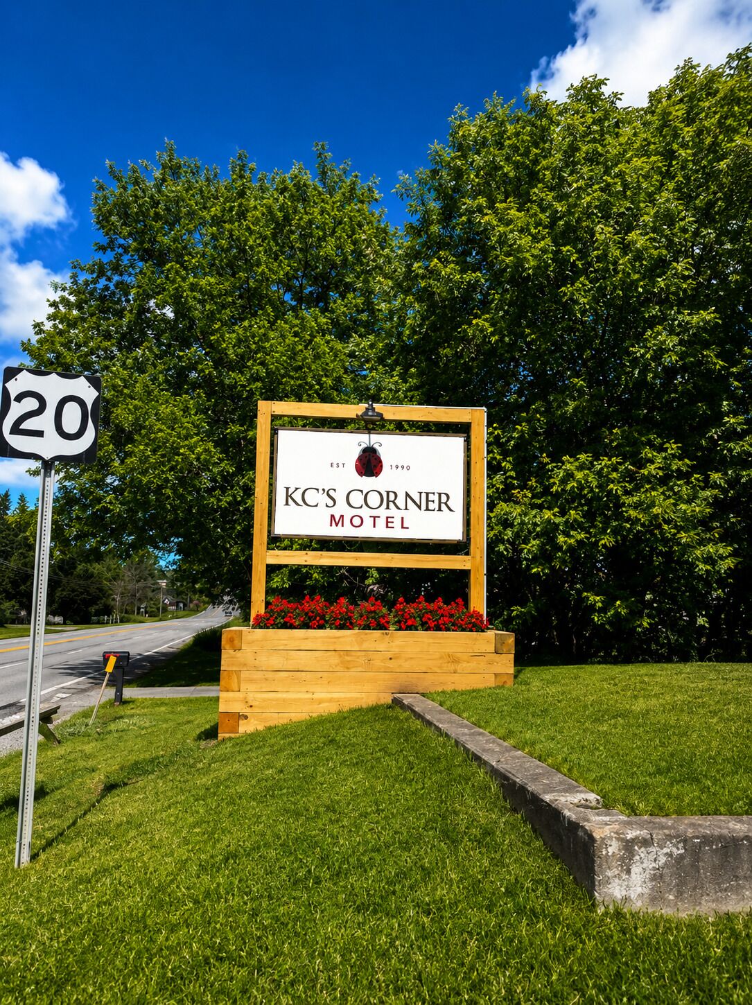 A motel sign with a wooden frame and a flower bed in front.