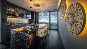 A modern kitchen with a marble island, pendant lights, and a view of a snowy landscape. - Crystal Pine Luxury Villas Jacuzzi&Sauna (Zakopane)
