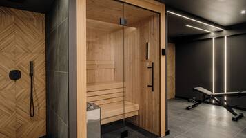 A modern sauna with wooden walls and a bench, a glass door, and a bench with weights in the adjacent room.