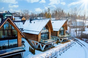 A modern cabin with large windows, a balcony, and a snowy landscape.