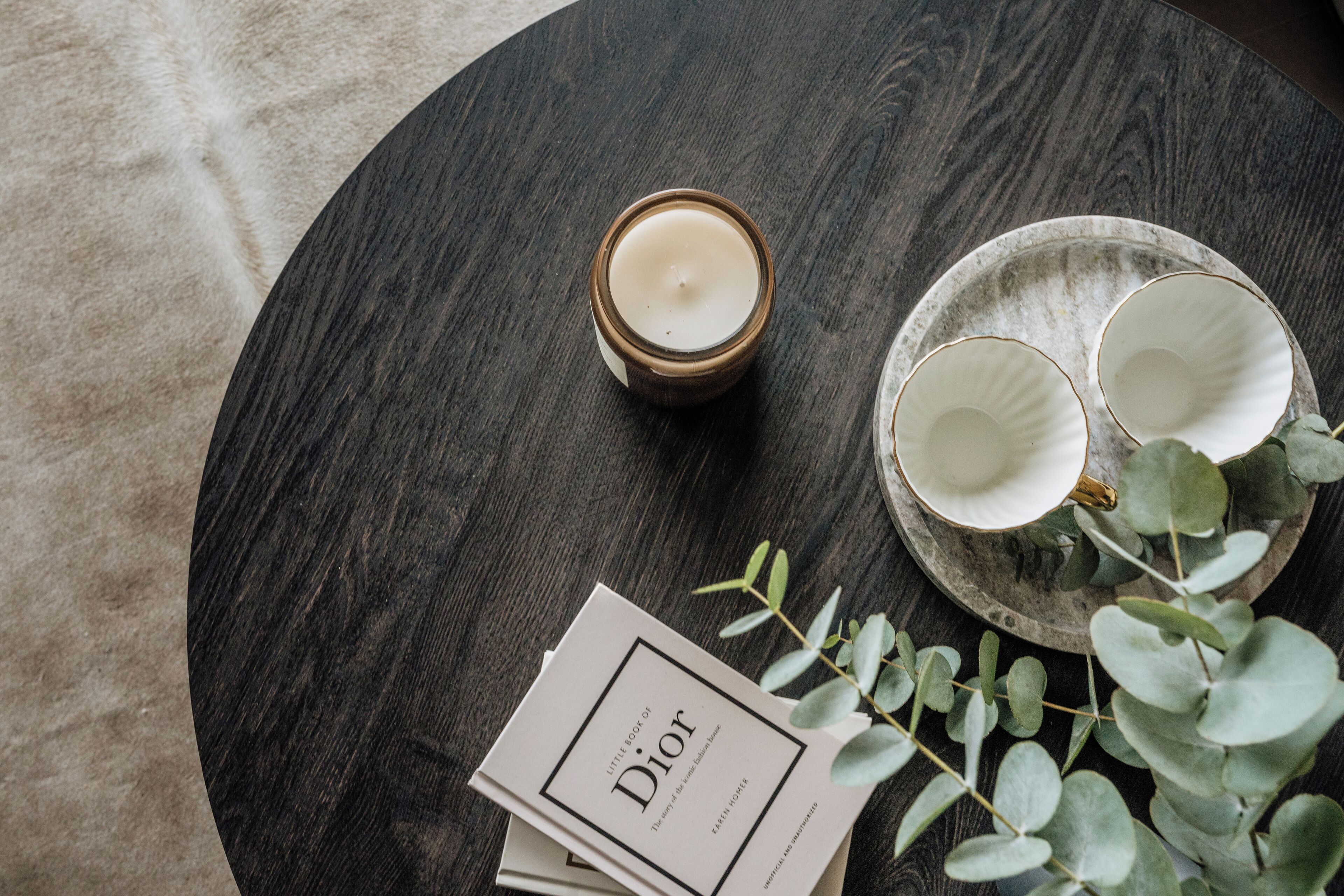 A round wooden table with a candle, two white cups, and a plate with leaves.