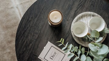 A round wooden table with a candle, two white cups, and a plate with leaves.