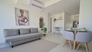 Ett modernt vardagsrum med en grå soffa, ett matbord med stolar, en köksdel och en stor spegel på väggen.
