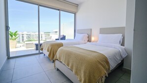 Ett hotellrum med två sängar, stora fönster och utsikt över staden.