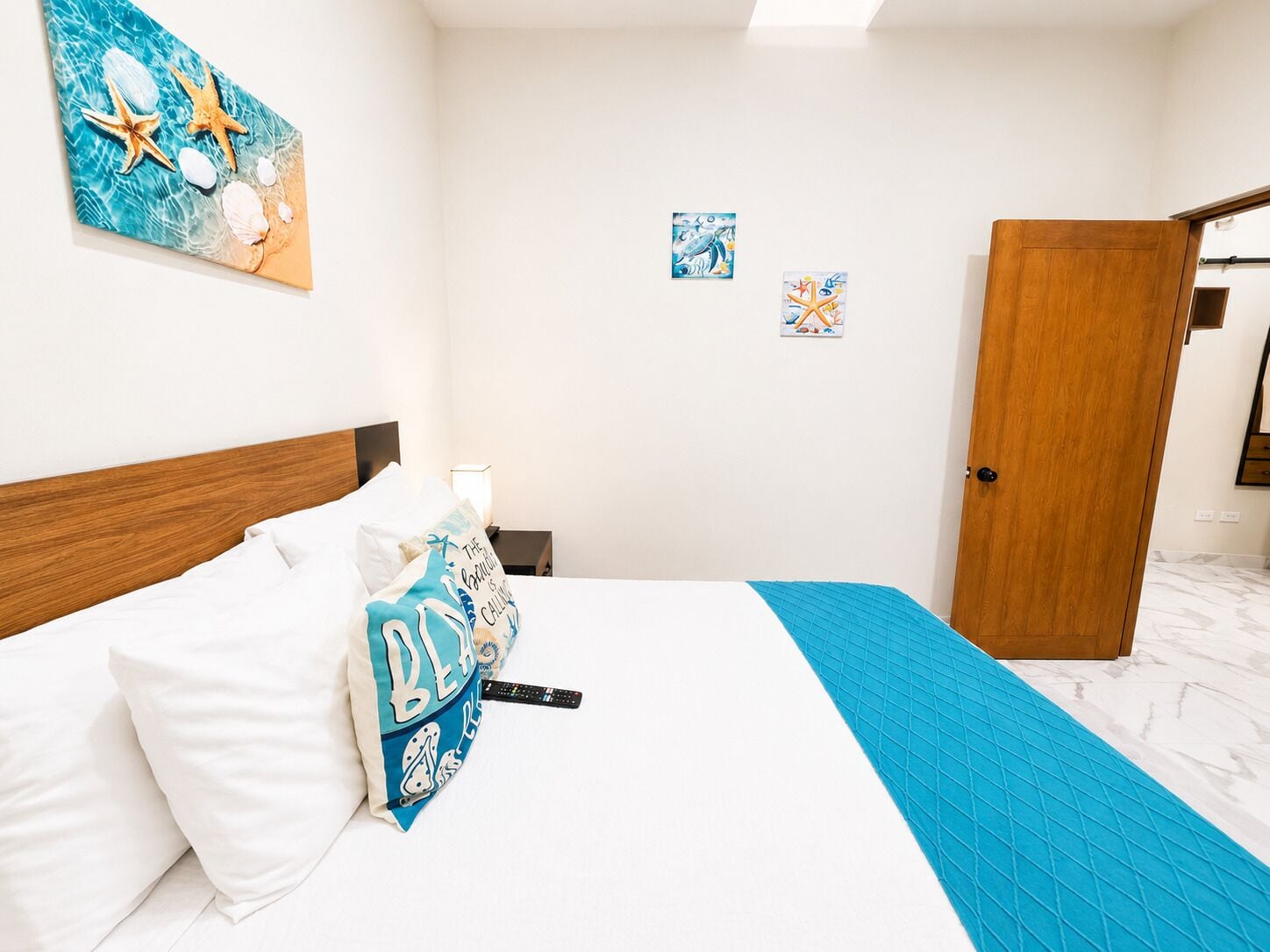 A hotel room with a bed, a wooden door, and two wall art pieces.