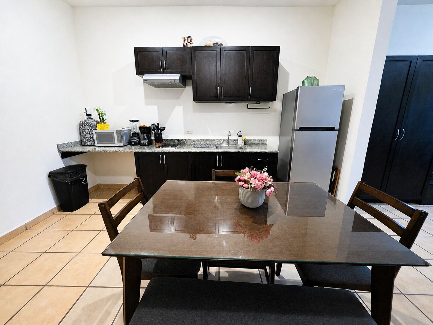 A compact kitchen with dark cabinets, a stainless steel refrigerator, a microwave, and a coffee maker on the countertop.