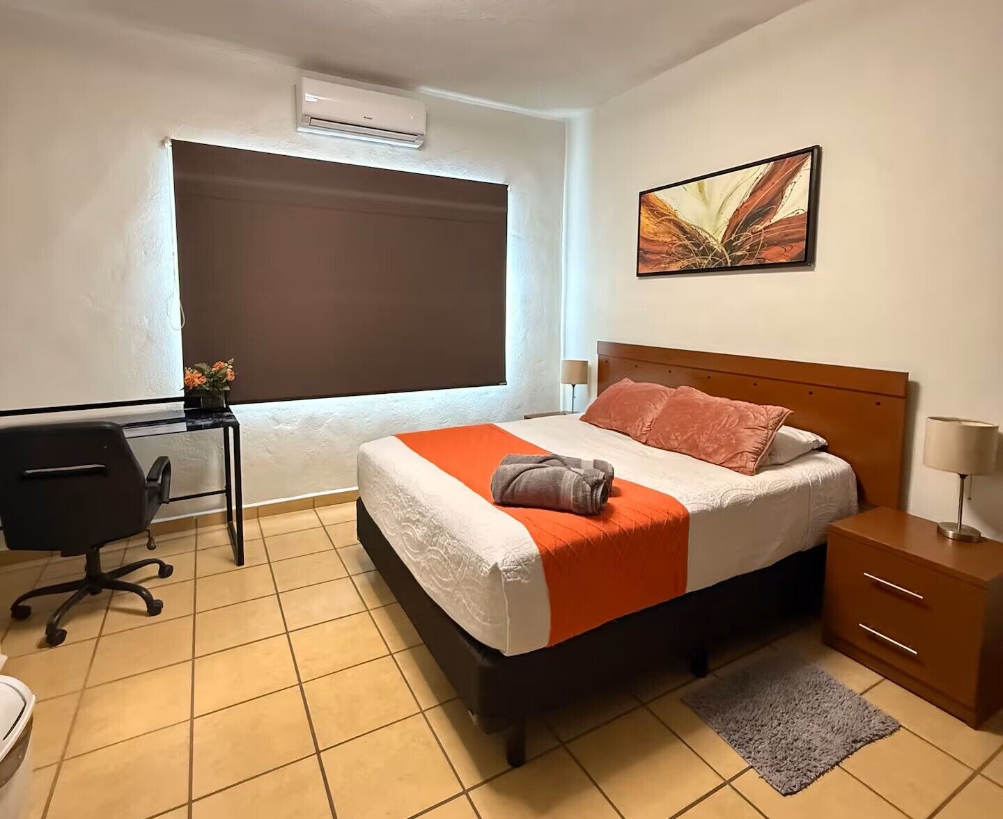 Een hotelkamer met een bed, bureau, stoel en een schilderij aan de muur.