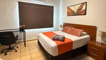 Een hotelkamer met een bed, bureau, stoel en een schilderij aan de muur.
