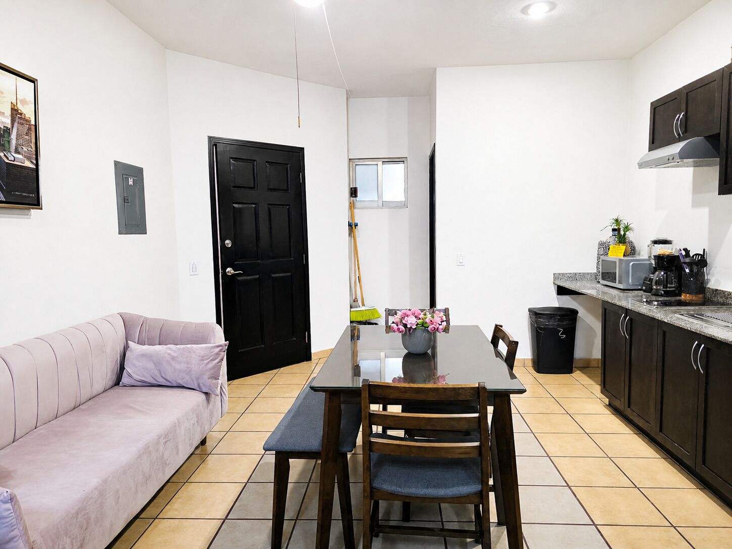 Un ambiente compatto con divano, tavolo da pranzo, sedie, angolo cottura dotato di mobili ed elettrodomestici, e una porta.