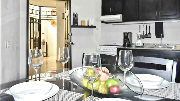 A dining area with a table set for two, a fruit bowl, and wine glasses. - Cabo Downtown Studios (Cabo San Lucas)