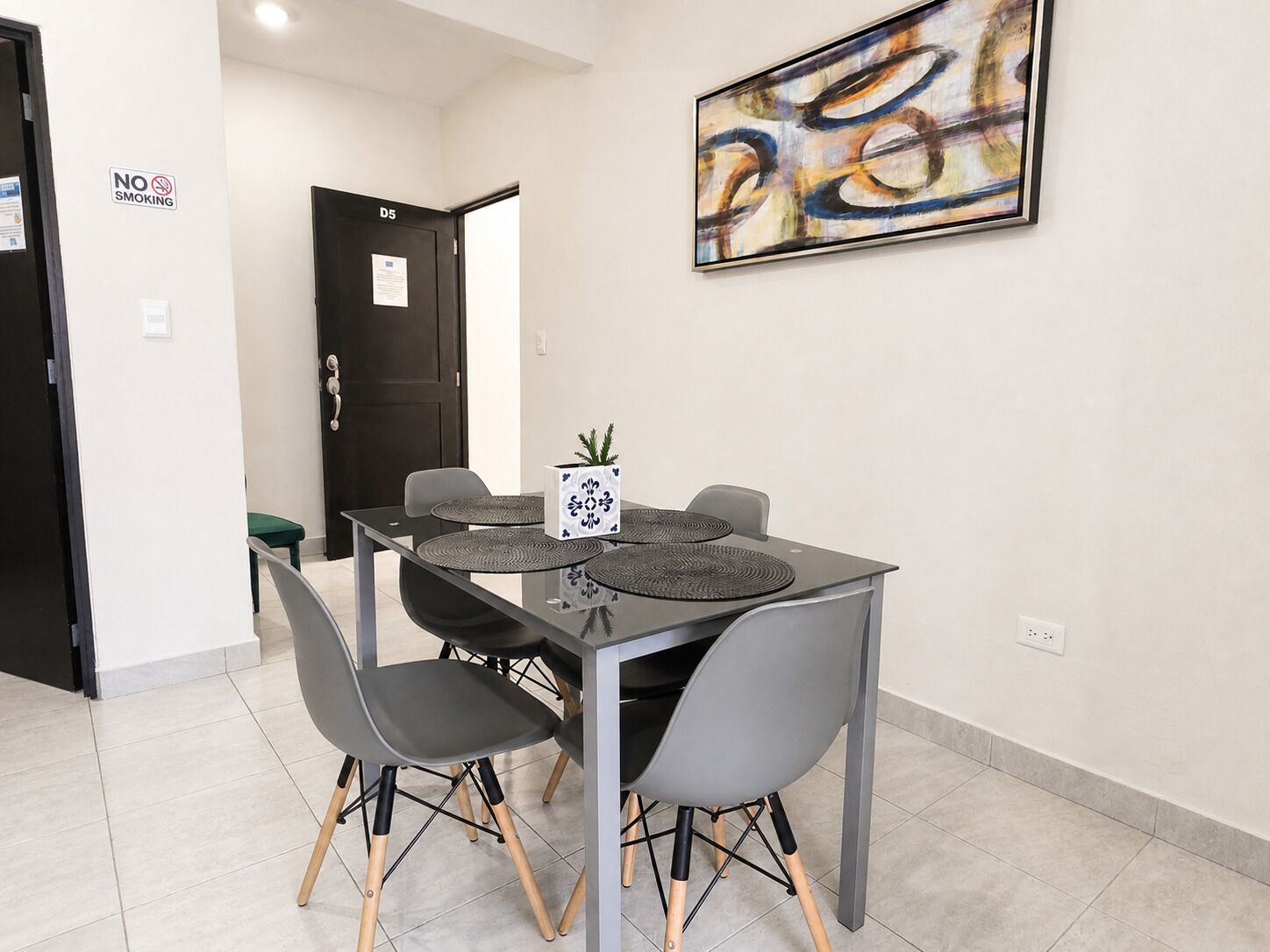 A conference room with a table, chairs, a plant, and a painting on the wall.