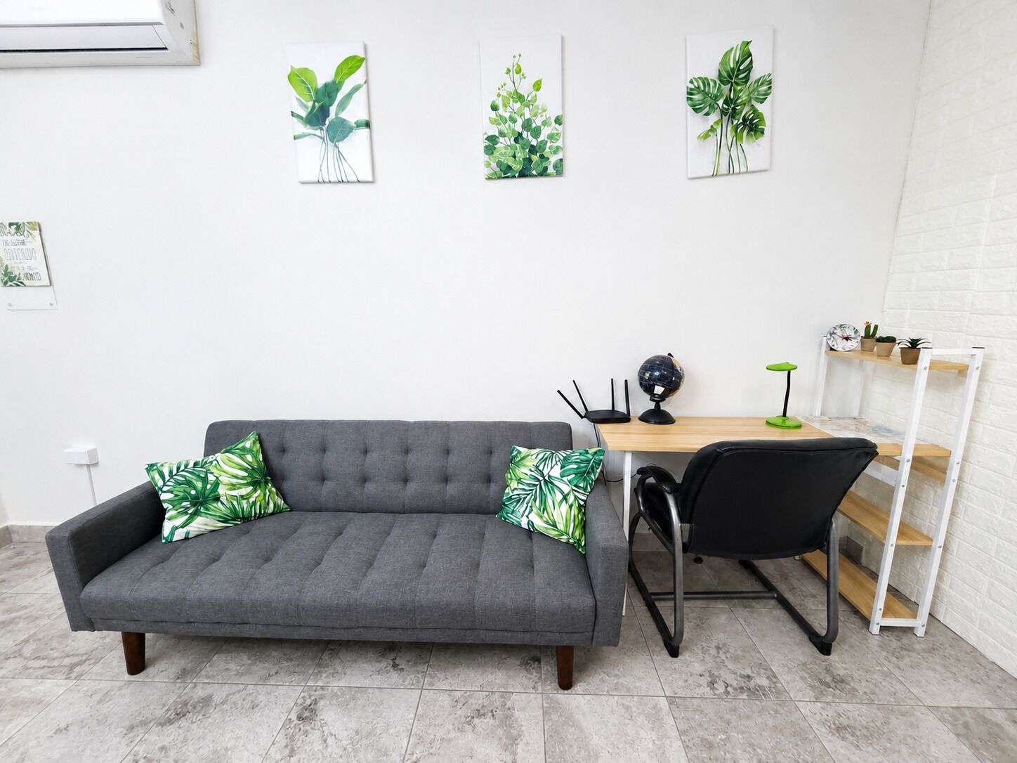 Una habitación moderna con un sofá gris, un escritorio de madera, una silla de oficina negra y tres obras de arte con plantas en la pared.