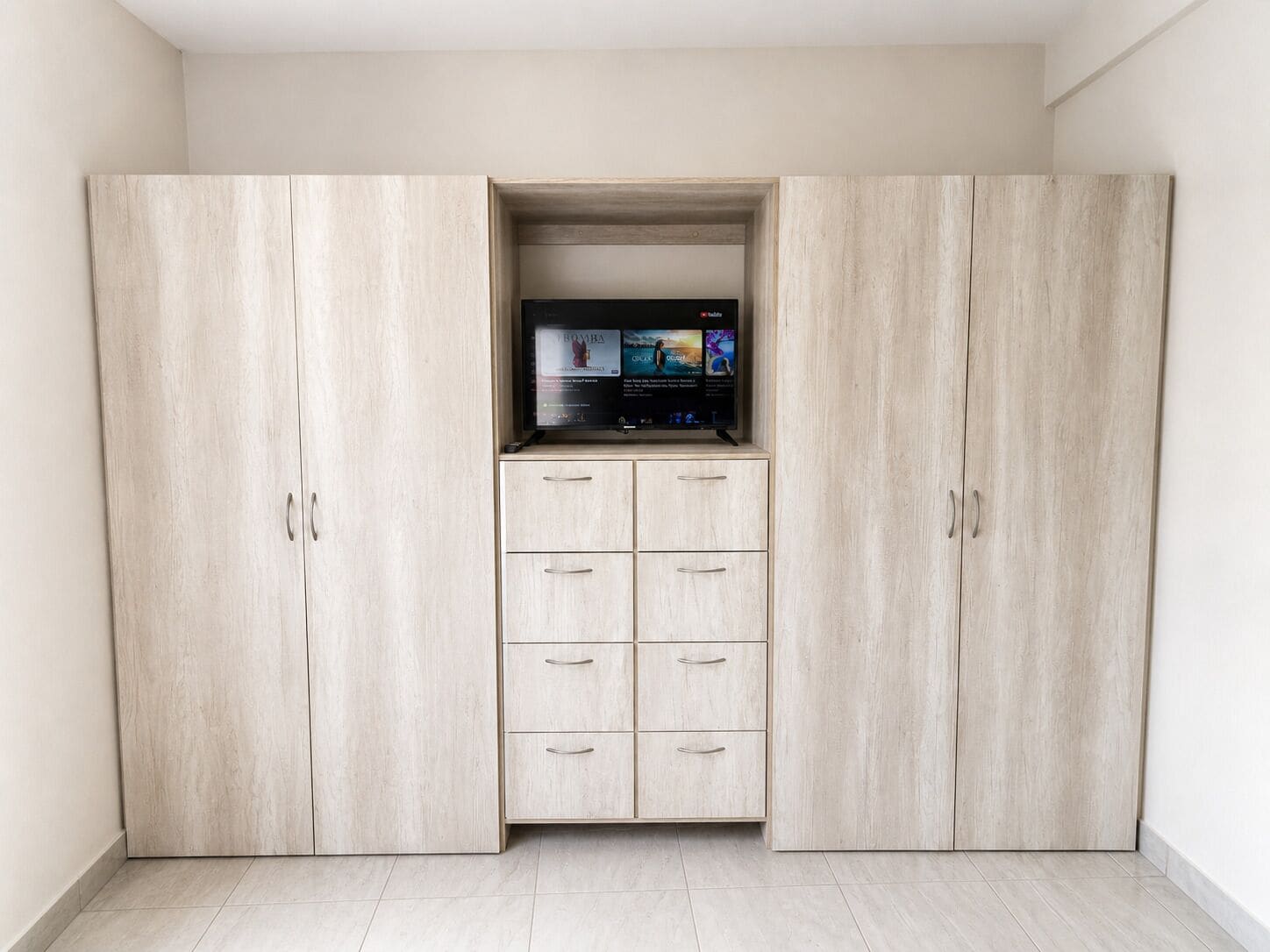 Una habitación con una estantería empotrada para el televisor, un armario con varios cajones y suelo de baldosas.