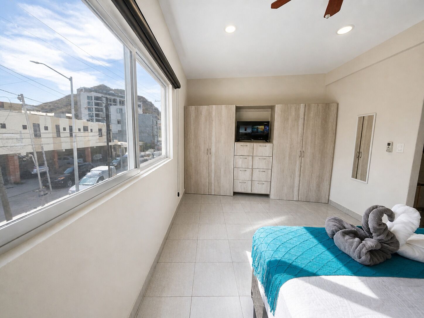 Un dormitorio con cama, televisor, armario y vista a la calle.