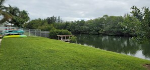 Un área verde con un cuerpo de agua, una terraza de madera y kayaks.