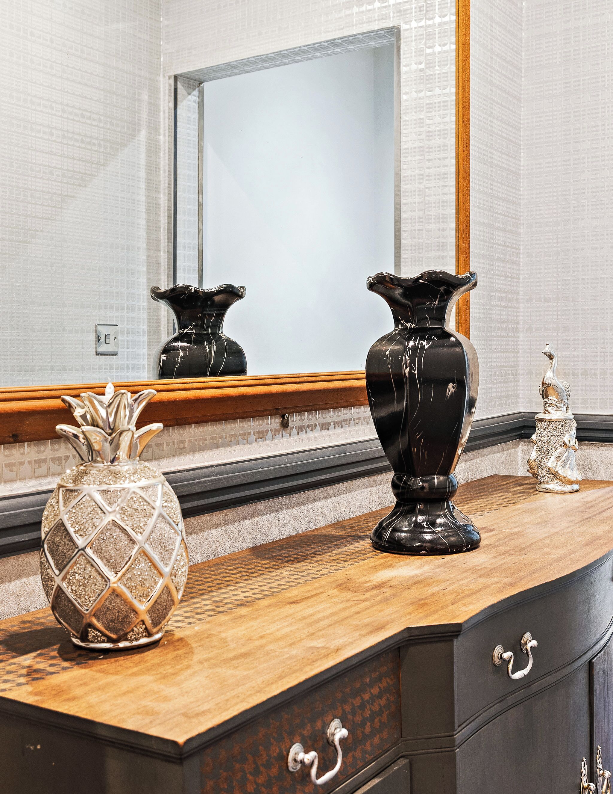 A bathroom vanity with a mirror, two black vases, and a pineapple-shaped vase.