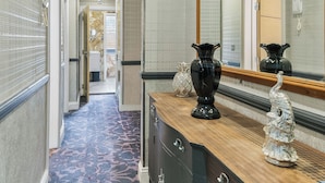 Um corredor de hotel com carpete estampado, uma toucador de madeira com espelho e um vaso decorativo.