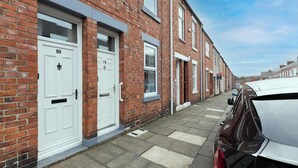 A row of red brick terraced houses with white doors, numbered 69 and 71, on a paved street.
