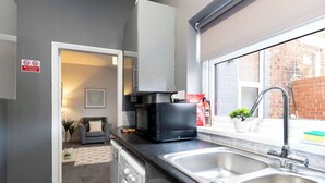 A compact kitchen with a microwave, sink, and a no-smoking sign.