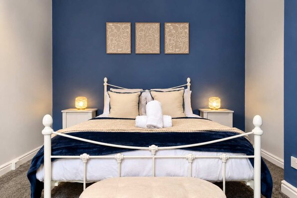 A bedroom with a bed, two bedside tables with lamps, a headboard, and three wall-mounted artworks.