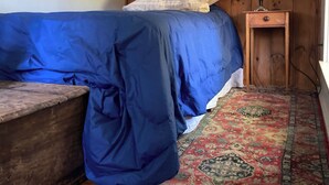 A small, cozy room with a single bed covered in blue bedding, a wooden headboard, a nightstand with a lamp, and a patterned rug on the floor. - The Boat Berth on Peaks Island (Portland)