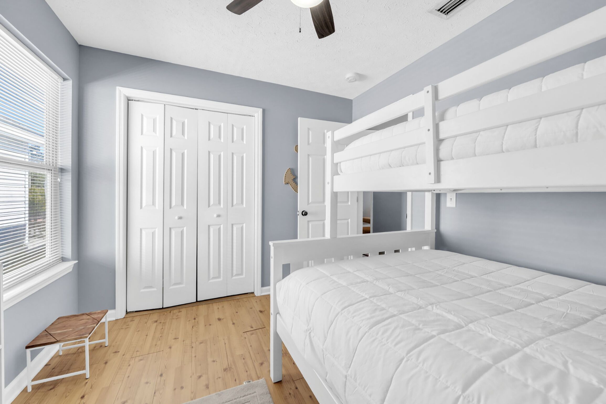 A bedroom with a bunk bed, a white door, and a window with blinds.