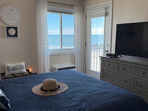 A bedroom with a view of the ocean, a bed with a blue quilt, a hat, a TV, and a 'NO WAKE ZONE' sign. - Best view of Ocean and Sunrise, relaxing beach area. (Myrtle Beach)