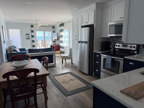 A modern kitchen with white cabinets, stainless steel appliances, and a dining area with a wooden table and chairs. - Best view of Ocean and Sunrise, relaxing beach area. (Myrtle Beach)