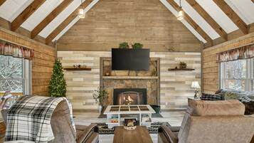 Un salon chaleureux avec une cheminée, des poutres en bois, un téléviseur et un sapin de Noël.