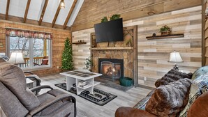 A cozy living room with a fireplace, wooden walls, a television, and a Christmas tree.