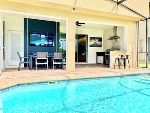 A swimming pool with a covered patio area, a flat-screen TV, and a dining setup. - Star Wars Loft  Themed Bedrooms, Private Pool, Summer Kitchen & PS5 (Kissimmee)
