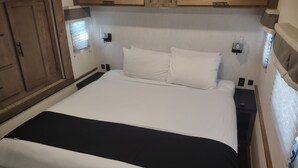 Un letto rifatto con biancheria bianco e nero, una testiera in legno e comodini con lampade.