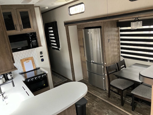 Cocina compacta con microondas, estufa y refrigerador de acero inoxidable. Cuenta con un comedor con mesa y sillas.