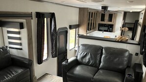 Interni di un camper compatto con angolo cottura, zona relax con divano e poltrone, e un piccolo oblò.