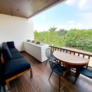 A balcony with a wooden table and chairs, a dark blue sofa, and a planter with small plants. - Very Central 2-Bedroom, 2 Bath Condo with WiFi, AC in Portside Puerto Morelos (Puerto Morelos)