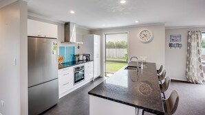 A modern kitchen with a stainless steel refrigerator, a built-in oven, and a large island with bar seating. - SeaRenity - Waimarama Holiday Home (Havelock North)