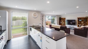 A modern kitchen with a large island, a dining area with a table and chairs, a TV, and a cozy seating area with sofas. - SeaRenity - Waimarama Holiday Home (Havelock North)